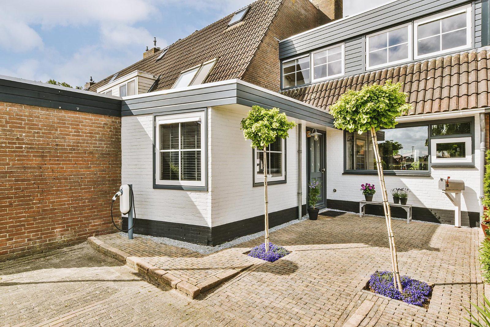 Witte aanbouw met platte overkapping en beplanting.