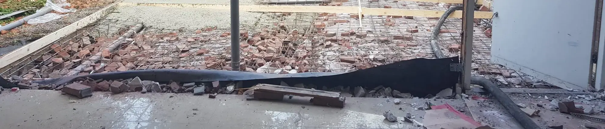 Wapening, puin en een gestorte betonvloer in een achtertuin, met de stortslang op de voorgrond.