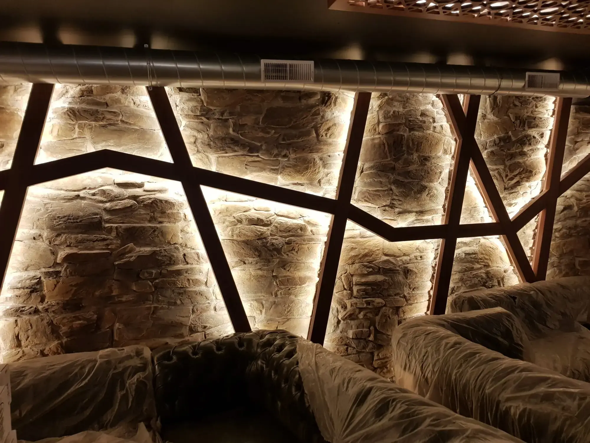 Stenen wand met verlichte houten lijsten in een horecazaak; de meubels staan nog in folie.