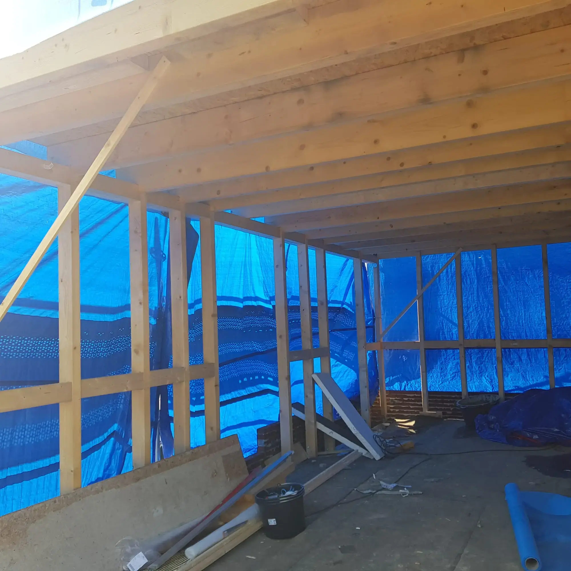 Binnenkant van een dakopbouw in aanbouw: houten balken en bouwzeil tegen de wind.